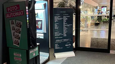 Fotoboks plassert i et kjøpesenter, med butikk i bakgrunnen.