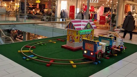 Lite lekeområde med togbanespor, hus og små figurer i kjøpesenter.