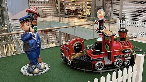 Skulptur av figur og liten rød togkarusell med hvitt gjerde rundt.