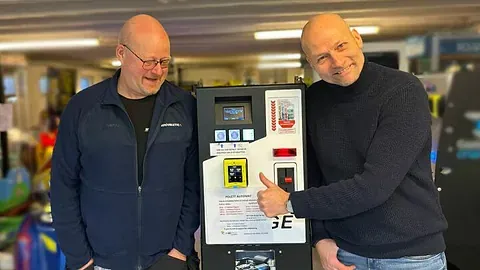 To smilende menn ved betalingsterminal.