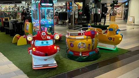 Røde og gule småfly og båtkarusell på grønt underlag i kjøpesenter.