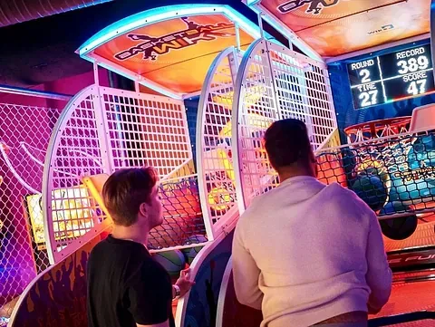 To menn spiller basketballspill på en fargerik arkademaskin.