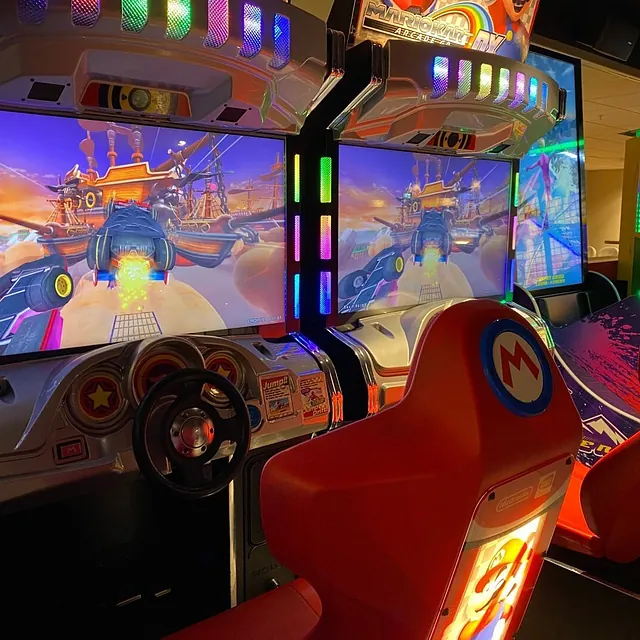 Lyst opp arkadespill med ratt og skjerm, plassert i en spillhall.