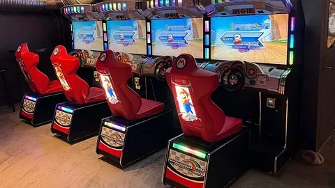 Mario bilspill med ratt og skjermer plassert tett i en mørk arkade.